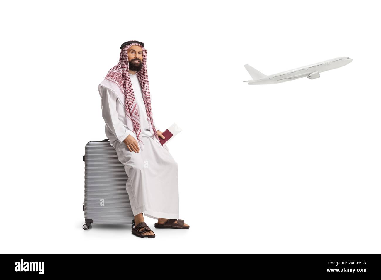 Homme arabe saoudien assis sur une valise avec passeport à la main et un avion décollant isolé sur fond blanc Banque D'Images