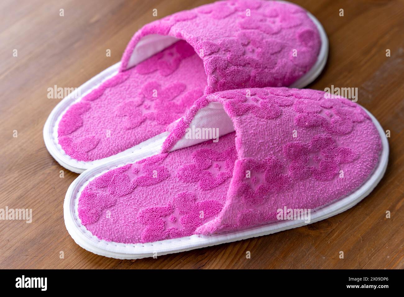 Une paire de pantoufles roses sont placées de manière décontractée sur un plancher en bois, créant une scène simple et confortable. Banque D'Images