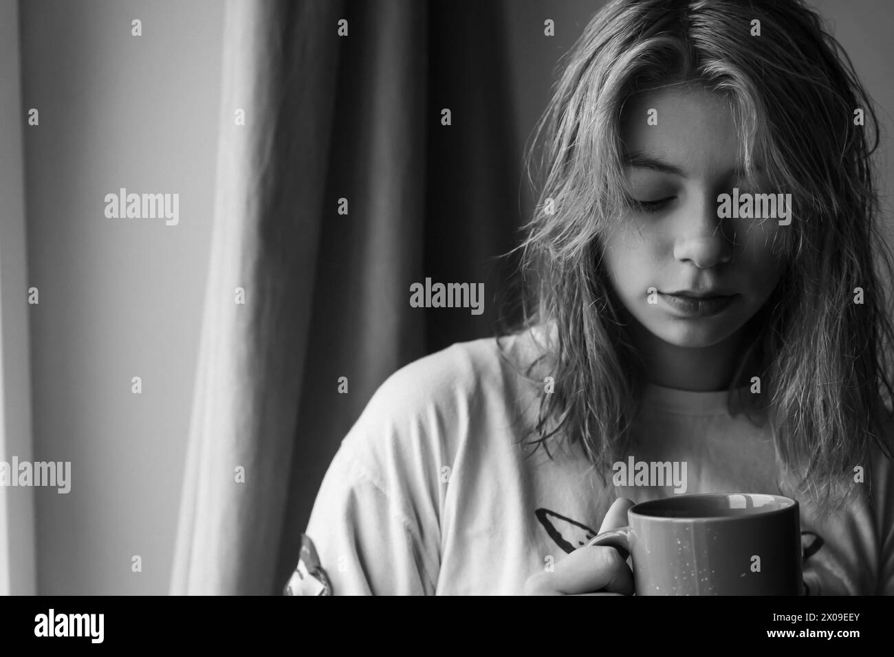 Une jeune fille de la génération Z, aux cheveux roux époustouflants, est assise près de la fenêtre, savourant une tasse de thé ou de café chaud. L'ambiance paisible et sa sére Banque D'Images