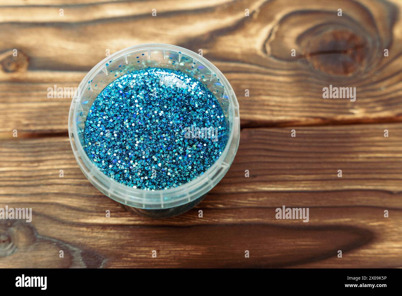 Un récipient aux paillettes bleues éclatantes se trouve au sommet d'une table en bois robuste, créant un contraste éblouissant de textures et de couleurs. slime Banque D'Images