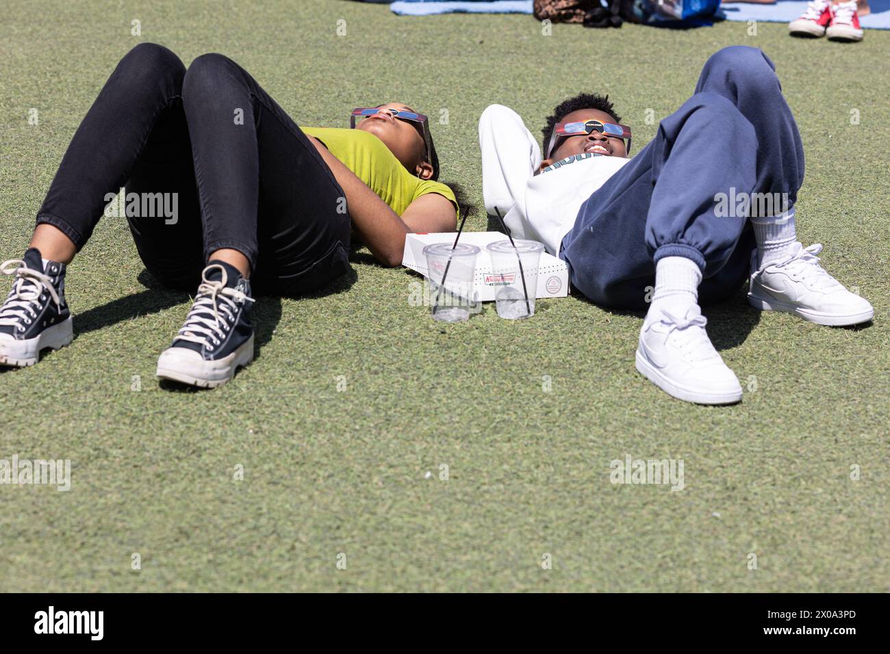 Atlanta, GA / USA - 8 avril 2024 : deux adolescents sont allongés sur le sol et regardent à travers des lunettes spéciales pour voir l'éclipse solaire totale du 8 avril 2024. Banque D'Images