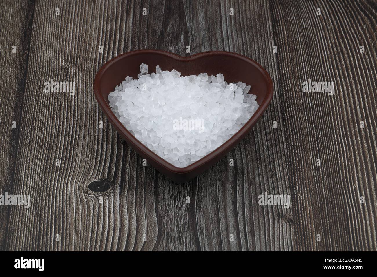 Sel de mer dans un bol en forme de coeur sur une table en pierre noire Banque D'Images