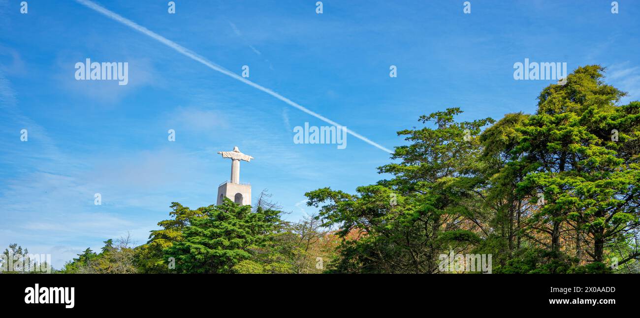 Statue du Christ d'Almada-Lisbonne, Portugal vue à travers la végétation avec un ciel bleu fort. Banque D'Images
