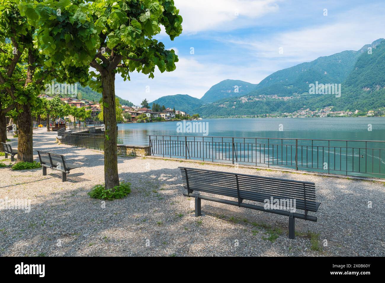 Parc avec bancs sur la rive d'un lac entouré de montagnes. Lac de Lugano et la ville de Riva San vitale, Suisse Banque D'Images