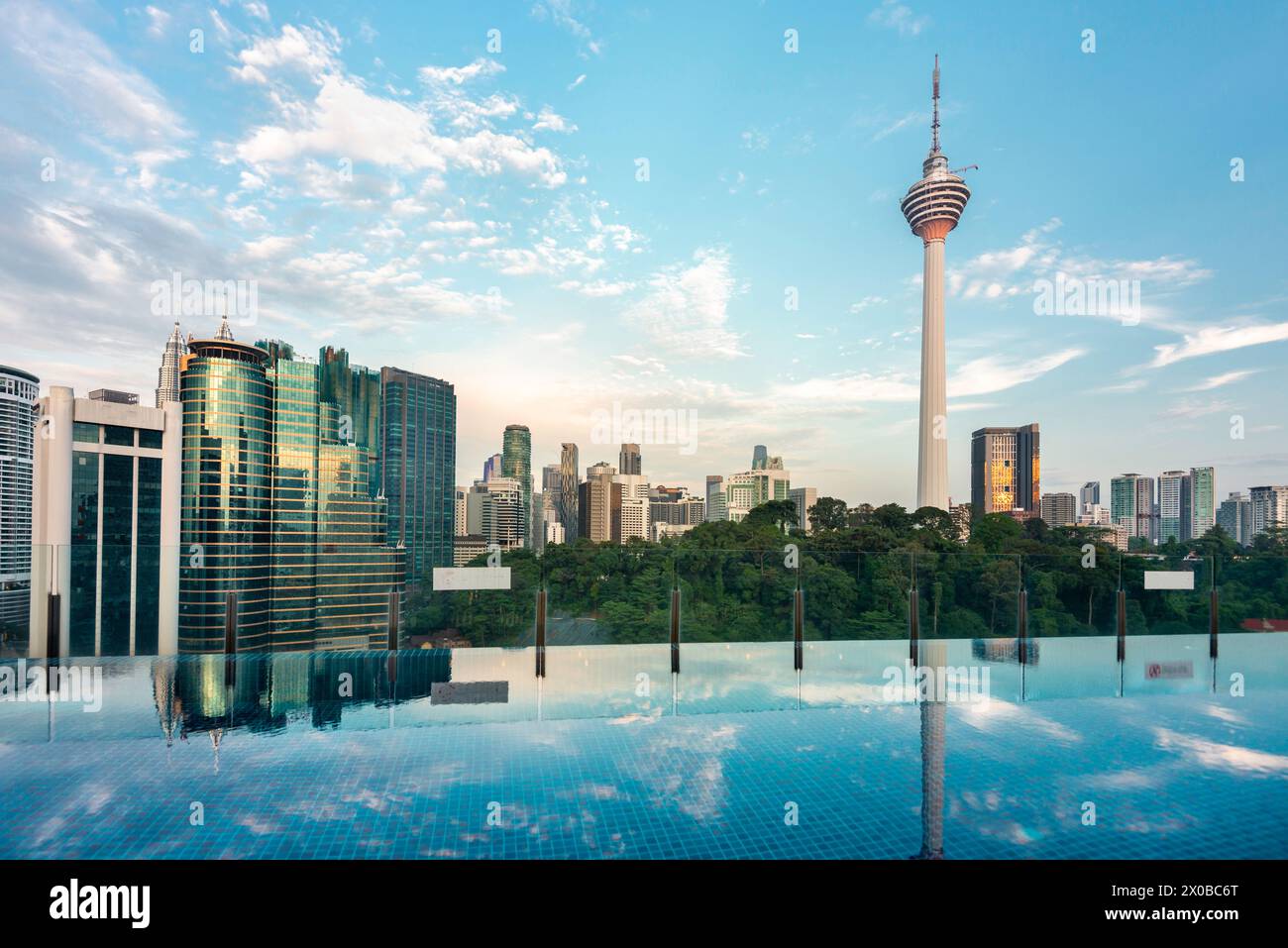 Superbe vue sur le toit de la ville de KL et Menara Kuala Lumpur, près du coucher du soleil avec bar bleu sur le toit piscine à débordement au premier plan et ciel bleu parsemé de Banque D'Images