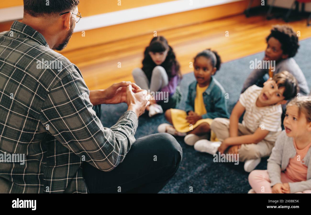 Éducateur enseigne une classe d'école primaire. Homme parlant devant un groupe d'enfants. Enseignant masculin donnant une leçon verbale de base, il enseigne aux enfants t Banque D'Images