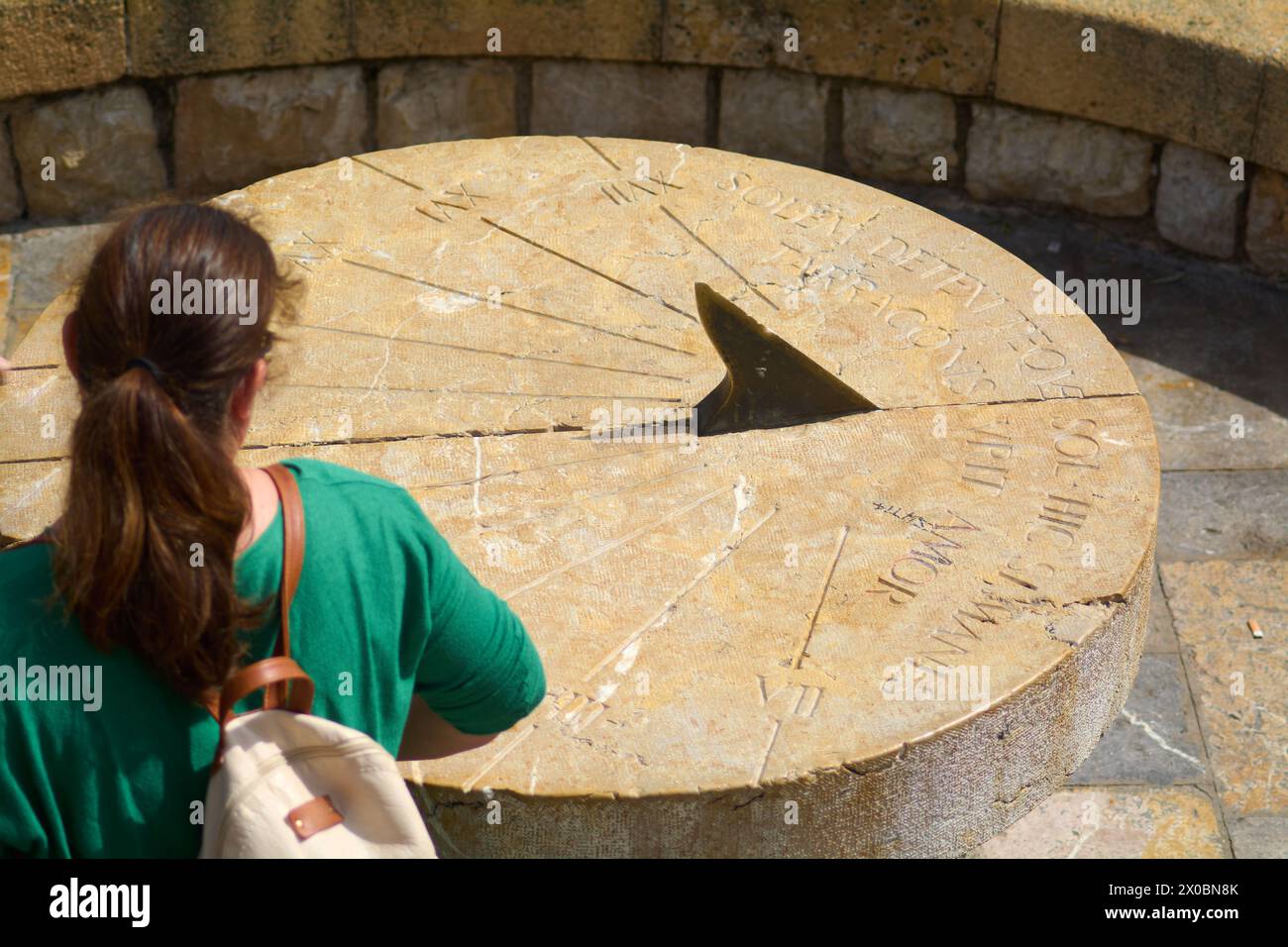 Vue arrière d'une femme méconnaissable contemplant un cadran solaire en pierre, avec des inscriptions érodées, dans un environnement naturel qui reflète l'histoire et m Banque D'Images