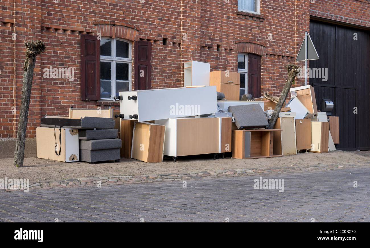 Pile de déchets encombrants avec des meubles sur le côté de la route devant une maison Banque D'Images