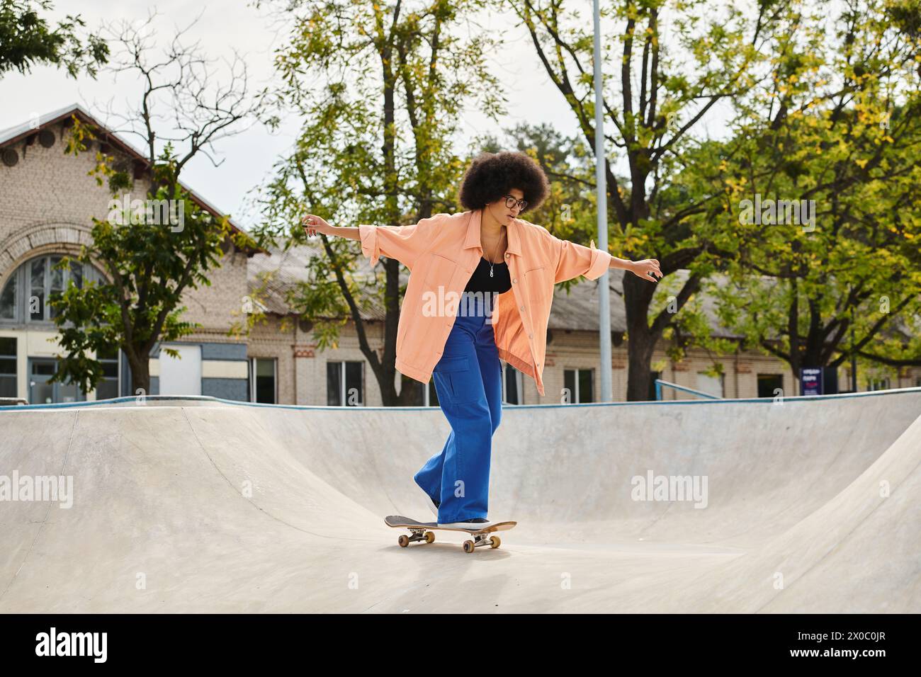 Une jeune femme afro-américaine aux cheveux bouclés monte une planche à roulettes sur le côté d'une rampe dans un skate Park en plein air. Banque D'Images