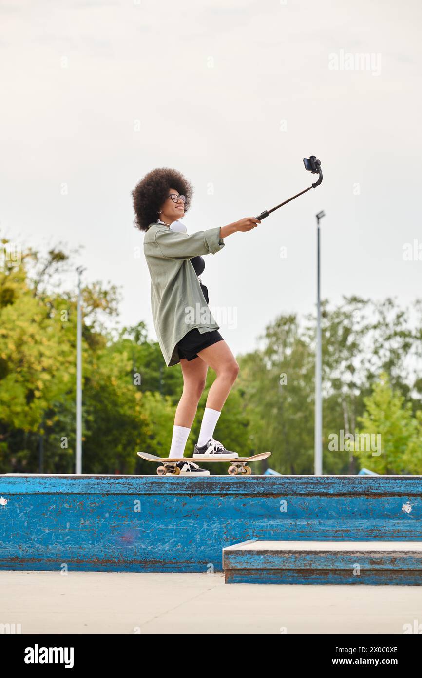 Une jeune femme afro-américaine aux cheveux bouclés glisse en douceur sur une rampe de skateboard dans un skate Park en plein air. Banque D'Images