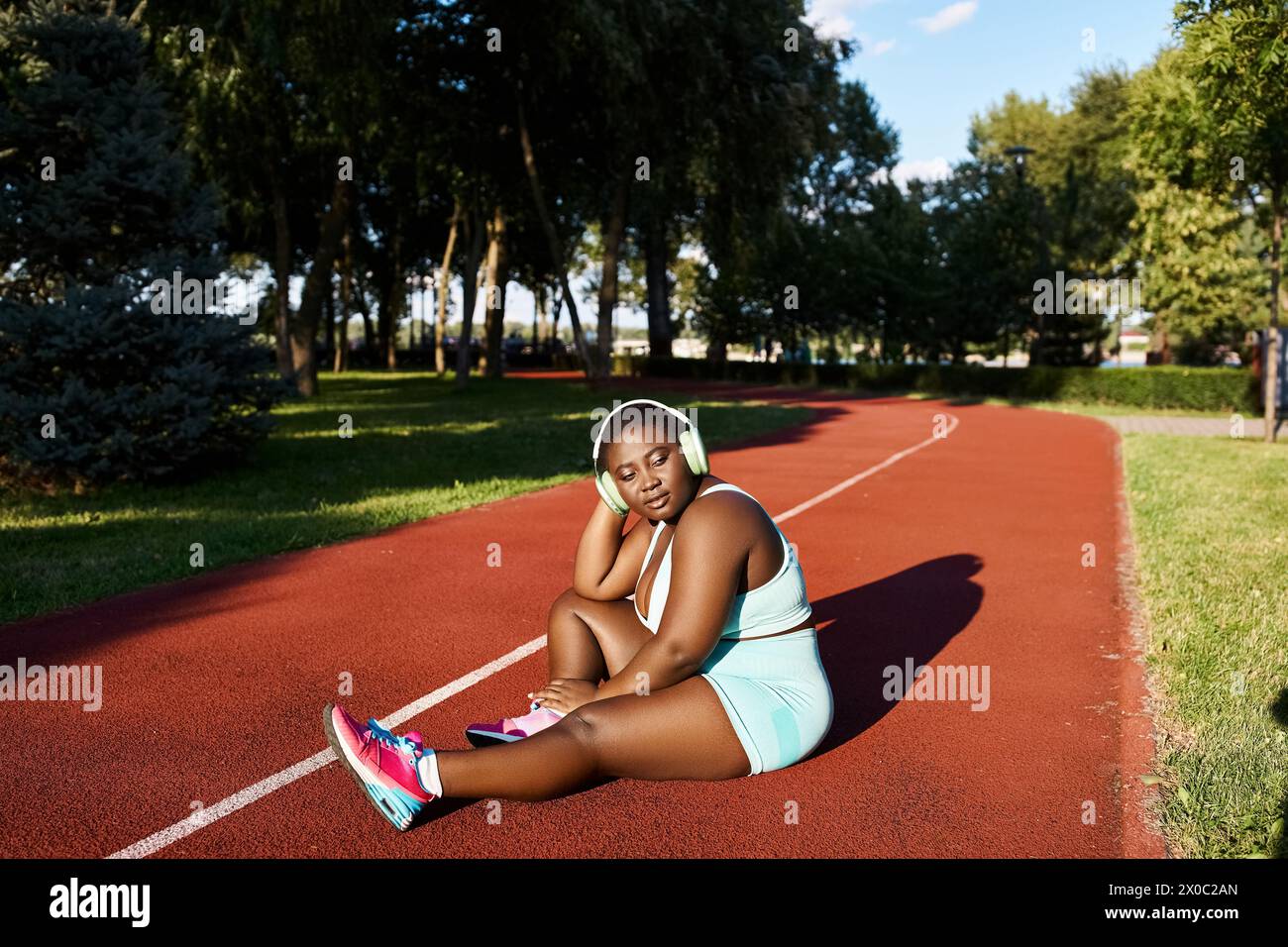 Une femme afro-américaine en vêtements de sport est assise sur un court de tennis, tenant une raquette en préparation d'un match. Banque D'Images