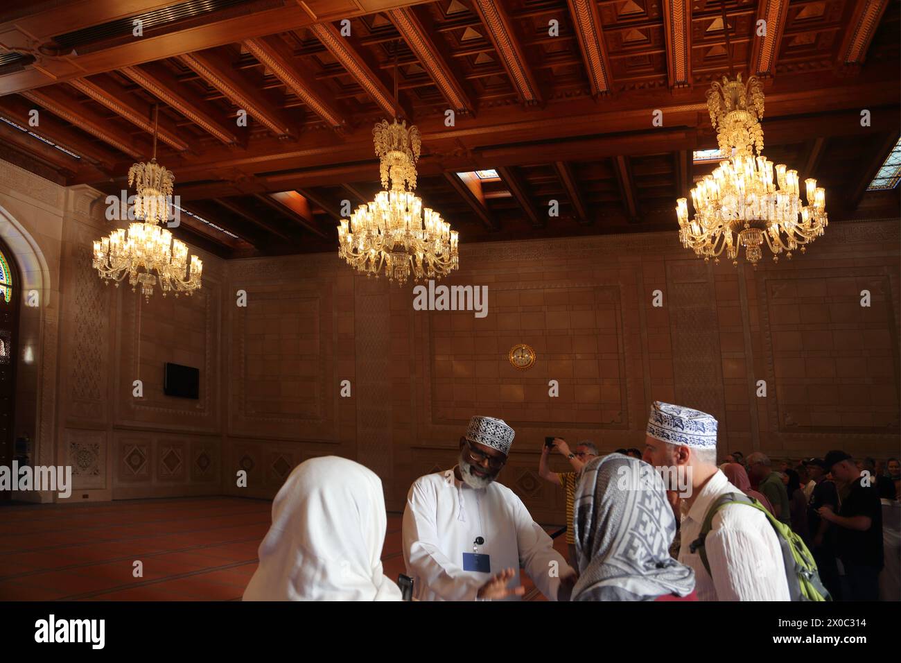 Guide touristique de la Grande Mosquée du sultan Qaboos avec des touristes dans la salle de prière des femmes avec plafond omanais en bois et lustres Muscat Oman Banque D'Images