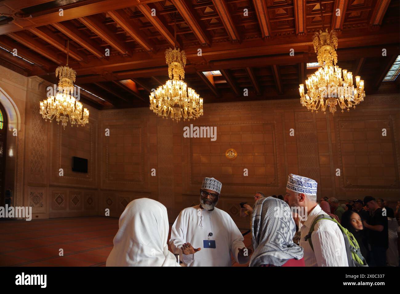 Guide touristique de la Grande Mosquée du sultan Qaboos avec des touristes dans la salle de prière des femmes avec plafond omanais en bois et lustres Muscat Oman Banque D'Images