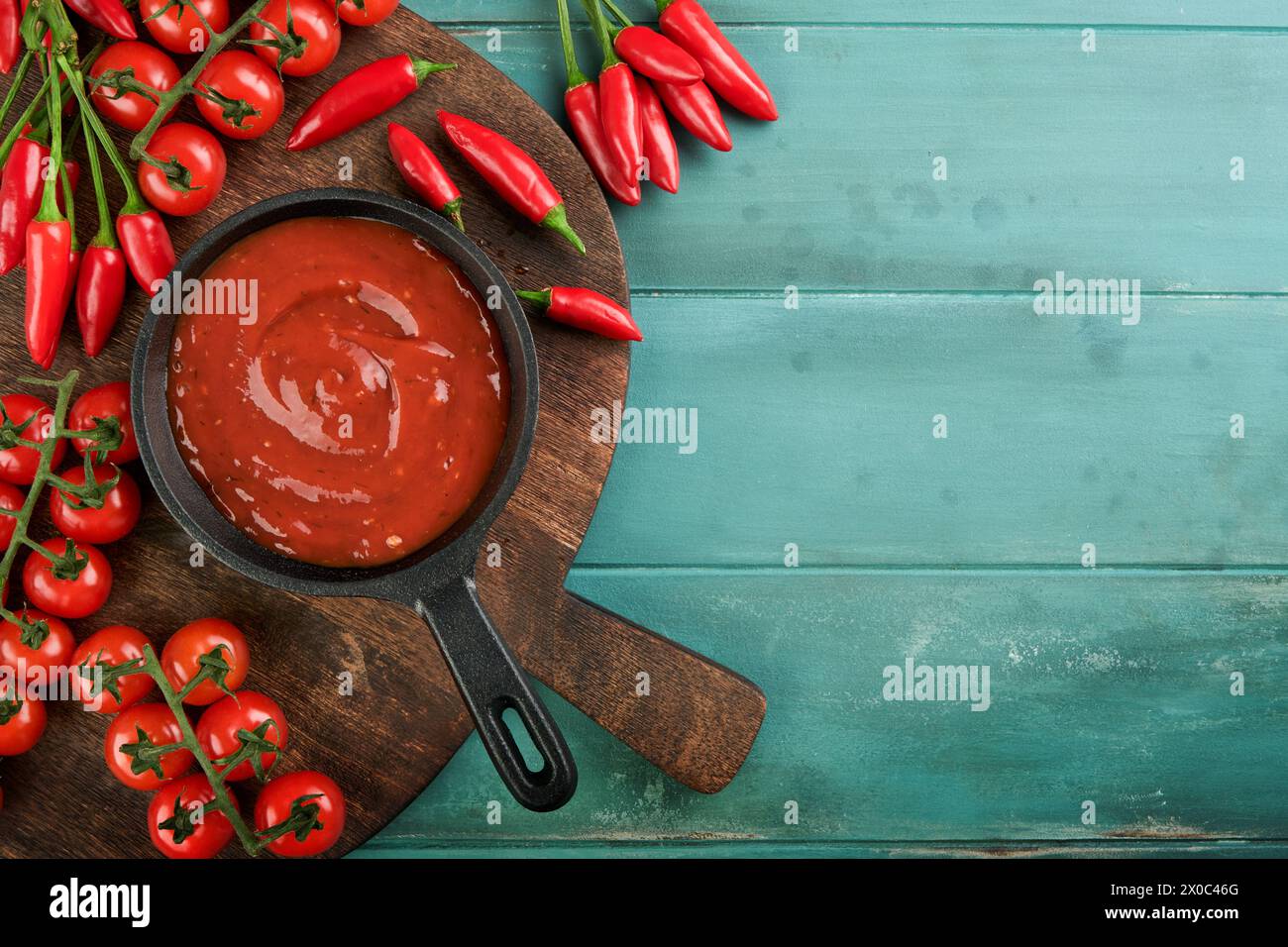 Sauce tomate italienne. Sauce tomate épicée maison ou ketchup avec tomate cerise et piment pour les pâtes et pizza dans une casserole vieille grotte rustique en bois Banque D'Images