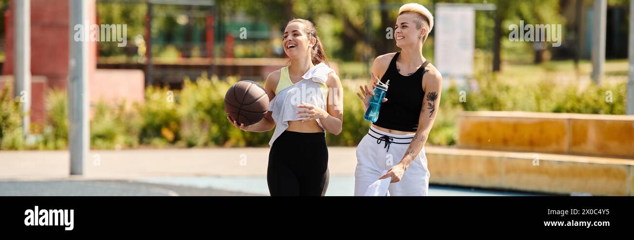 Deux jeunes femmes athlétiques, amies, se tiennent côte à côte sur le terrain de basket-ball, profitant d'une journée d'été à faire du sport. Banque D'Images