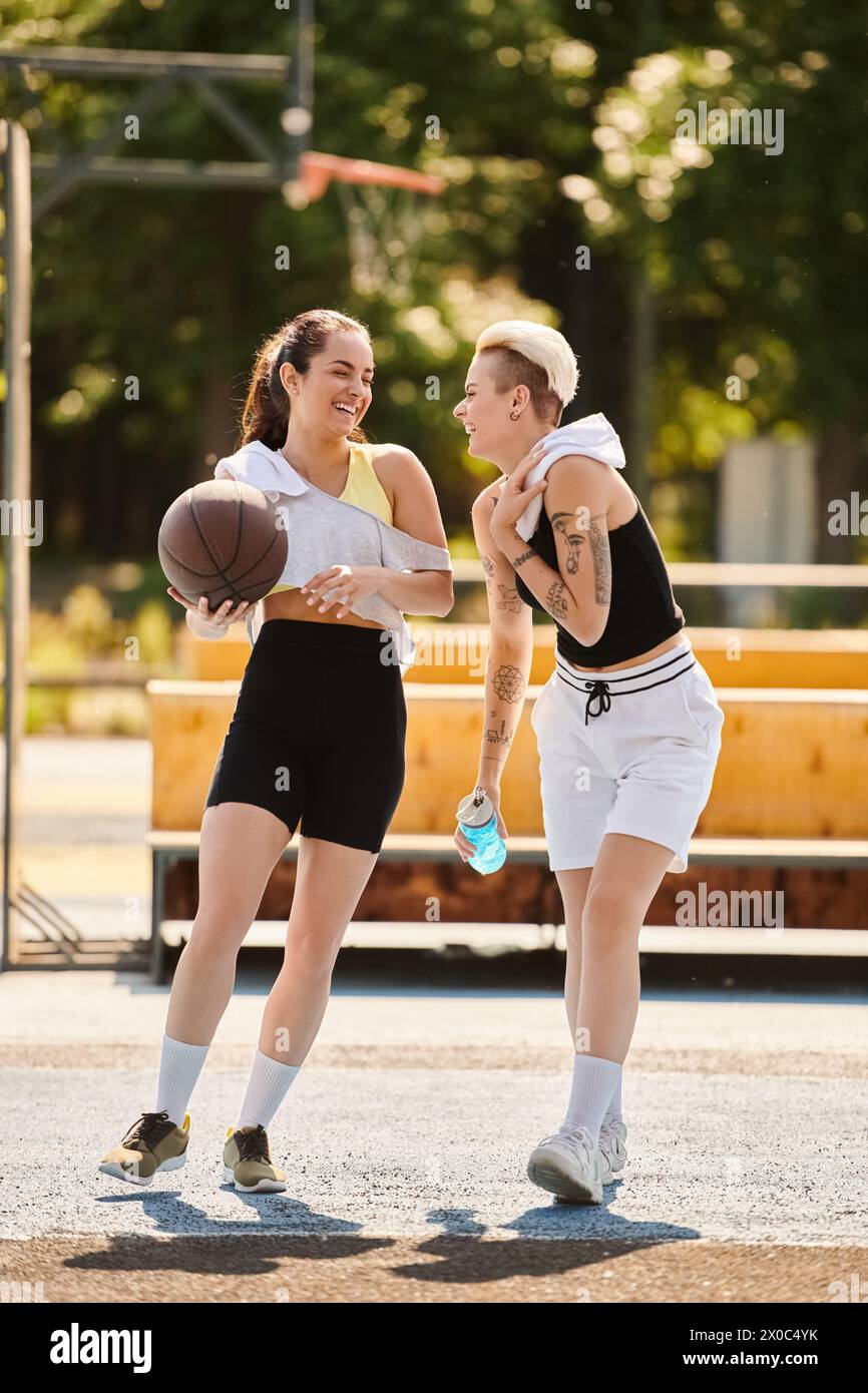 Deux jeunes femmes athlétiques dribbles et cerceaux de tir sur un terrain de basket-ball extérieur ensoleillé en été. Banque D'Images