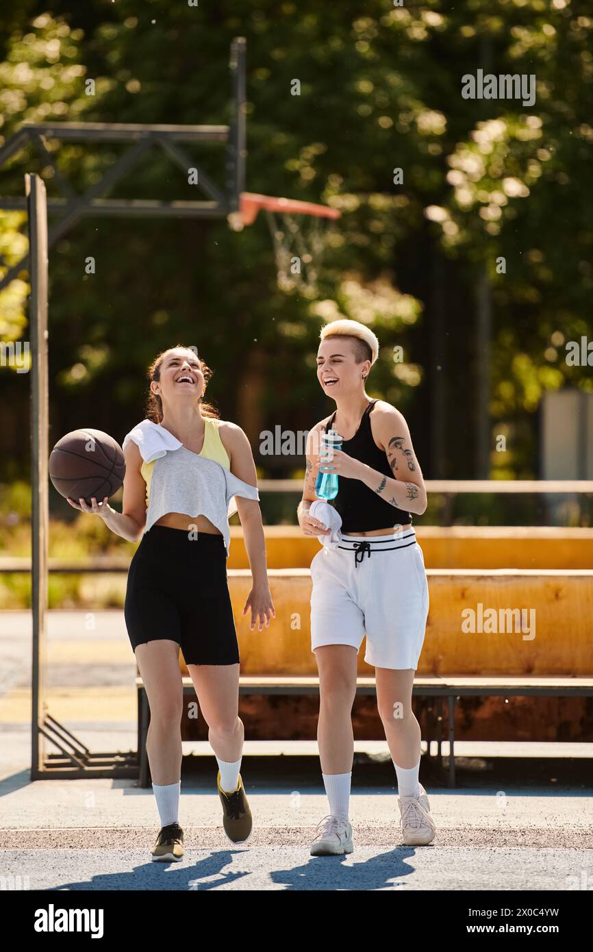 Jeunes femmes athlétiques jouant au basket-ball ensemble à l'extérieur par une journée ensoleillée, mettant en valeur le travail d'équipe et l'amitié. Banque D'Images