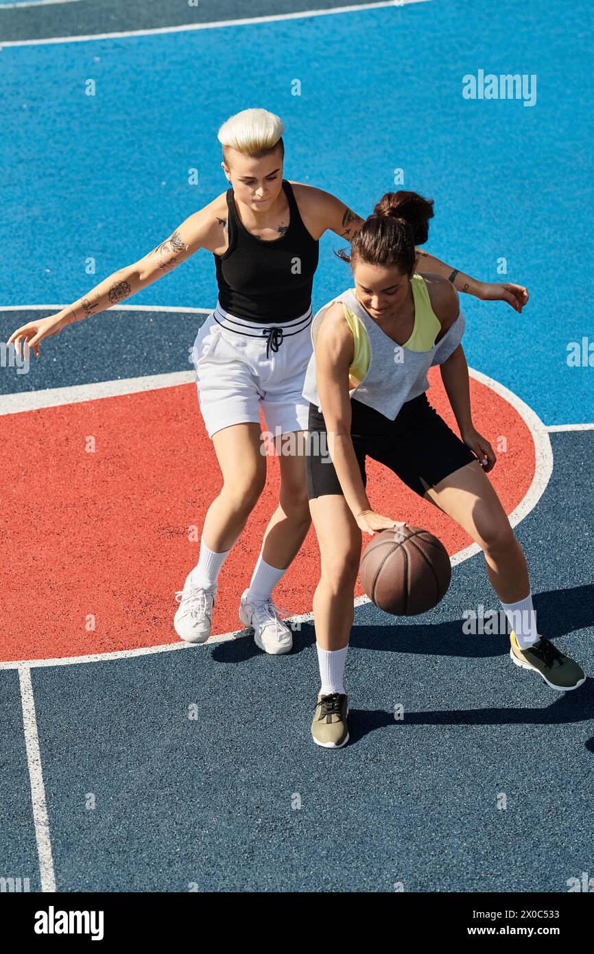 Deux jeunes femmes, amies et athlètes, engagées dans une partie compétitive de basket-ball sur un terrain extérieur en été. Banque D'Images