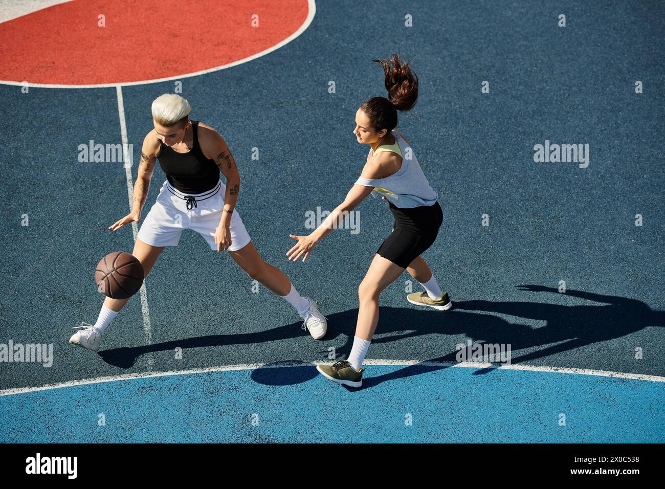 Deux jeunes femmes athlétiques se tiennent triomphalement au sommet d'un terrain de basket-ball sous le soleil d'été. Banque D'Images