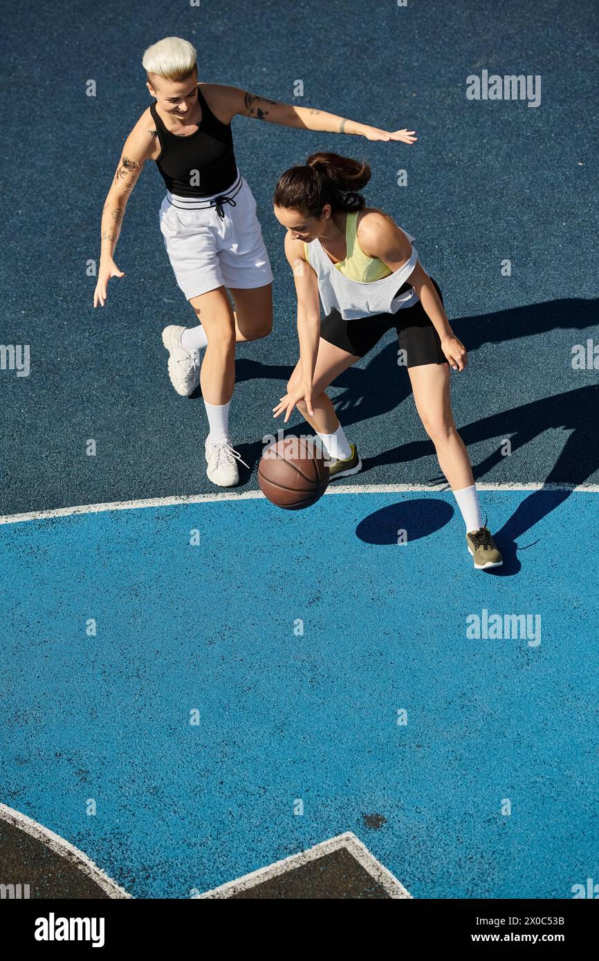 Deux amies sportives sont immergées dans un match de basket-ball compétitif sur un terrain extérieur pendant l'été. Banque D'Images