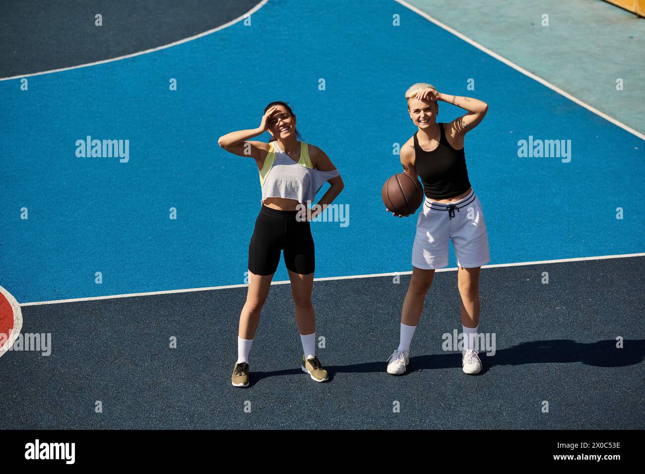 Deux femmes athlétiques se tiennent fièrement au sommet d'un terrain de basket-ball, incarnant la force et l'amitié dans le soleil d'été. Banque D'Images