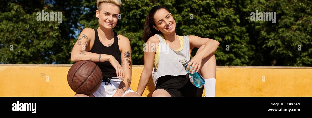 Deux jeunes femmes en tenue sportive sont assises sur un terrain de basket-ball, discutant et profitant d'une pause détente après avoir joué un match. Banque D'Images