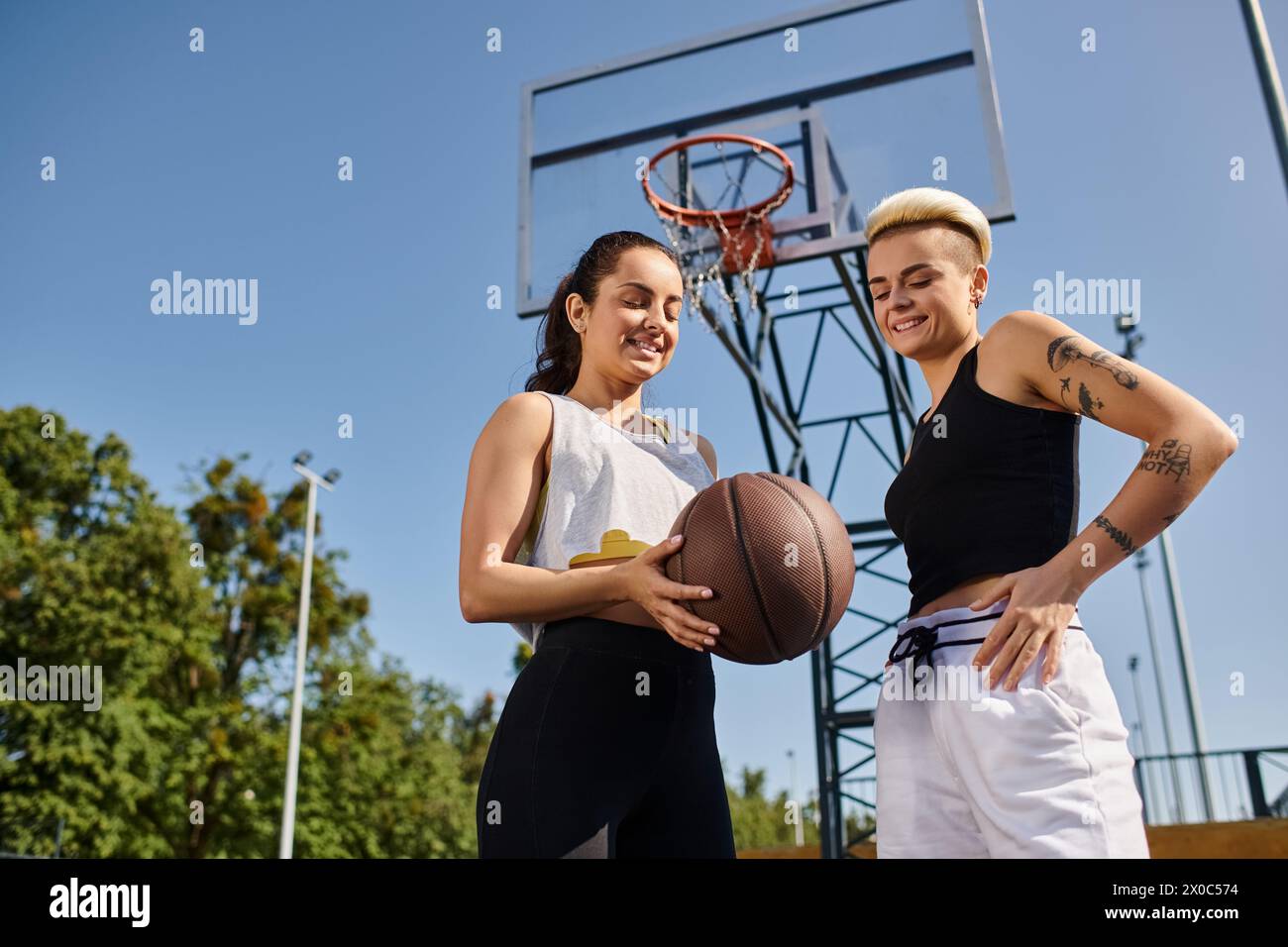Deux jeunes femmes athlétiques dribblant un basket-ball en plein air par une journée ensoleillée, profitant d'un match amical ensemble. Banque D'Images