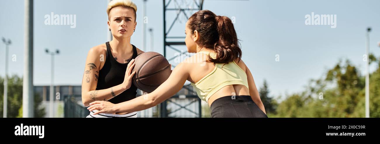 Deux jeunes femmes athlétiques profitent d'un match de basket-ball ensemble à l'extérieur par une journée ensoleillée. Banque D'Images