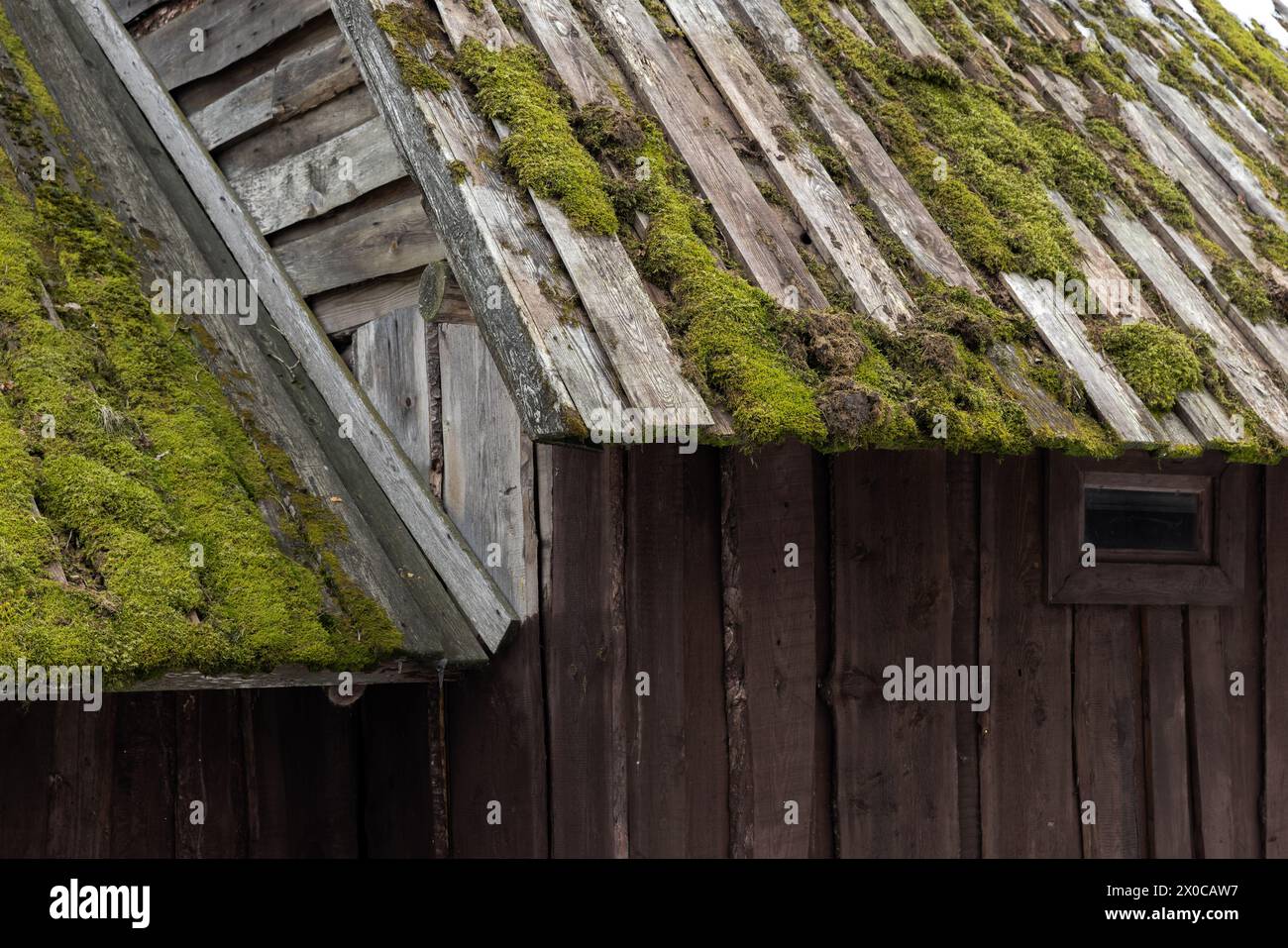 Détails extérieurs de la vieille maison en bois. Toit avec mousse verte et murs faits de planches grises rugueuses, texture de photo de fond Banque D'Images