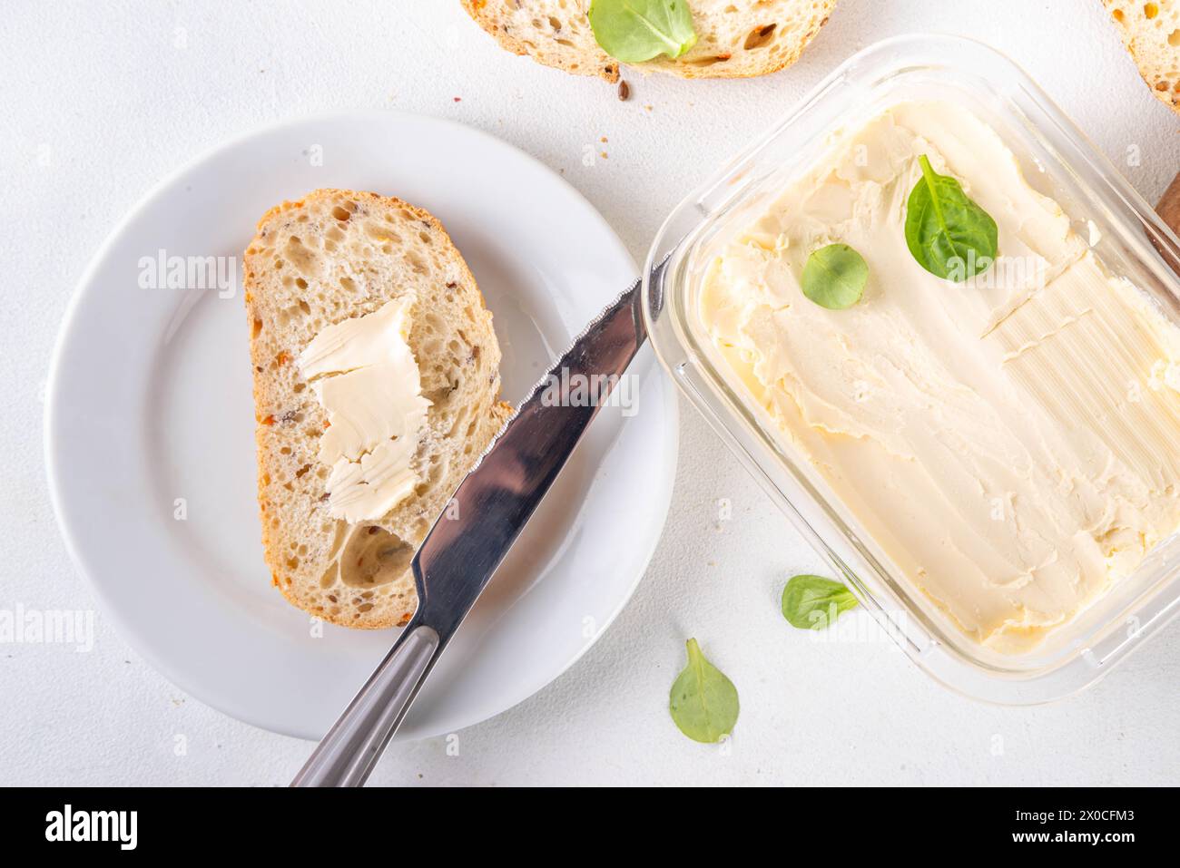 Beurre végétalien maison, crémeux non laitier, beurre alternatif à base de plantes avec de la feuille de soja, et pain cuit à la maison sur fond de table blanc de cuisine Banque D'Images