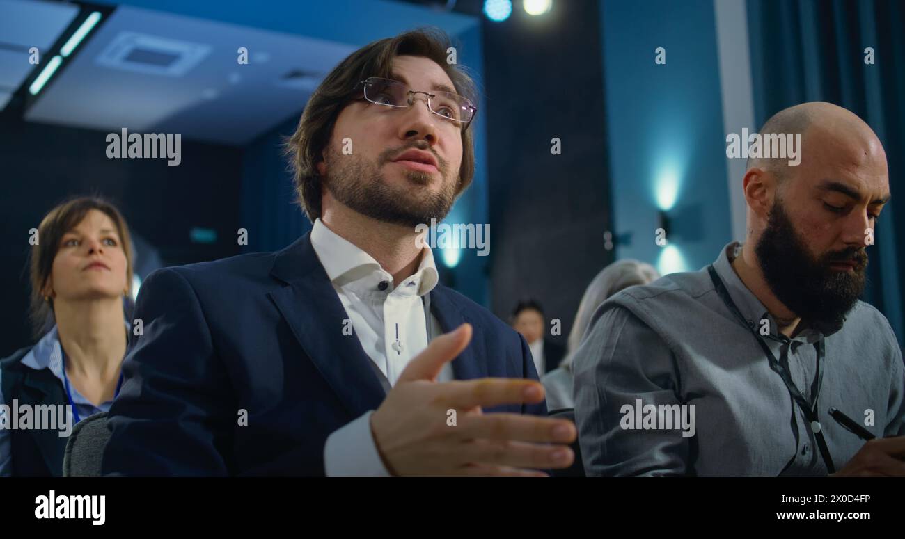 Divers travailleurs des médias lèvent la main, écrivent les réponses dans des cahiers du représentant de l'organisation pendant la campagne de presse dans la salle de conférence. Un journaliste masculin caucasien pose une question lors de l'interview. Banque D'Images