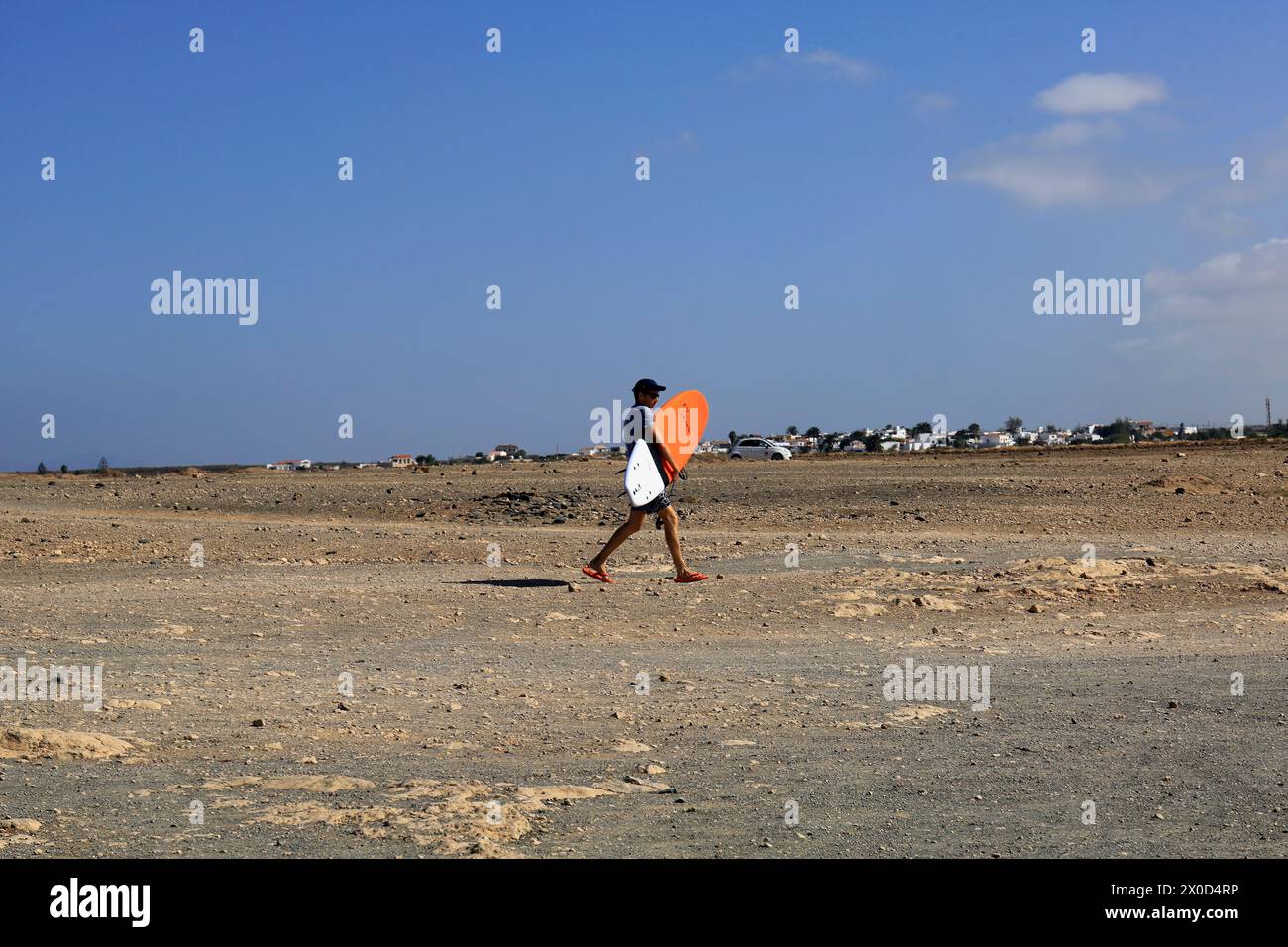 Homme portant une planche de surf à travers le terrain découvert, El Cotillo, Fuerteventura. Prise en février 2024 Banque D'Images