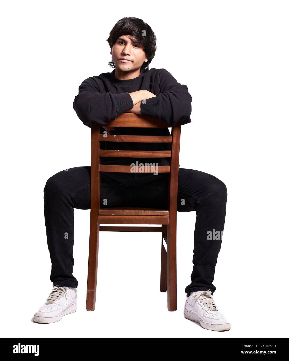 Un homme est assis sur une chaise en bois, les bras croisés. Il porte une chemise noire et un pantalon noir. La chaise est brune et a des lattes en bois. Le ma Banque D'Images
