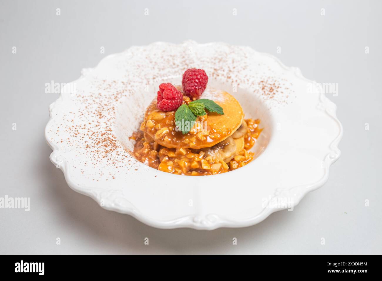 Crêpes moelleuses avec des framboises et des feuilles de menthe sur une plaque blanche sur un fond blanc propre. Gros plan. Banque D'Images
