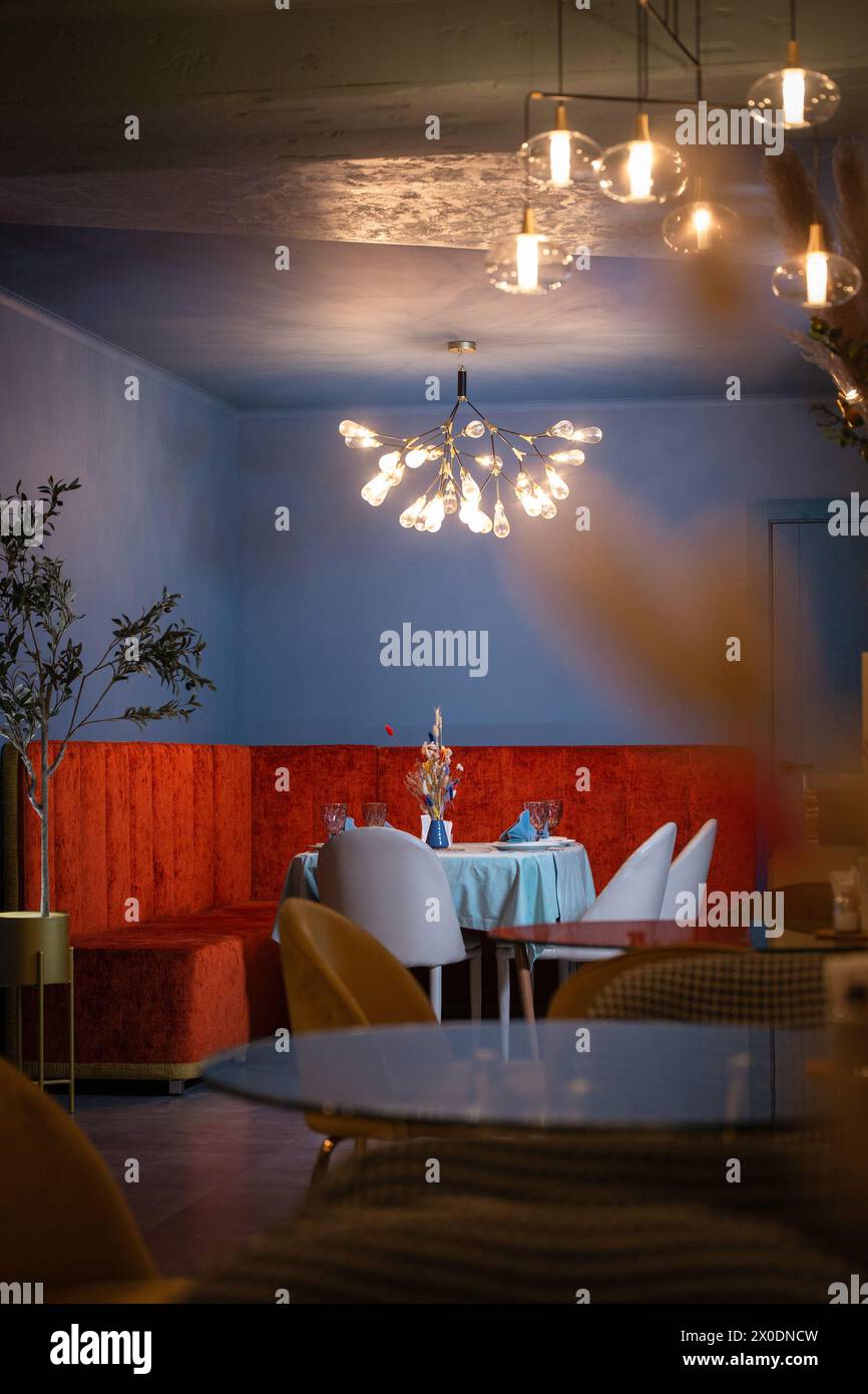 Un bel intérieur de restaurant avec des murs bleus et des meubles en velours rouge. Le restaurant est éclairé par un beau lustre. Banque D'Images