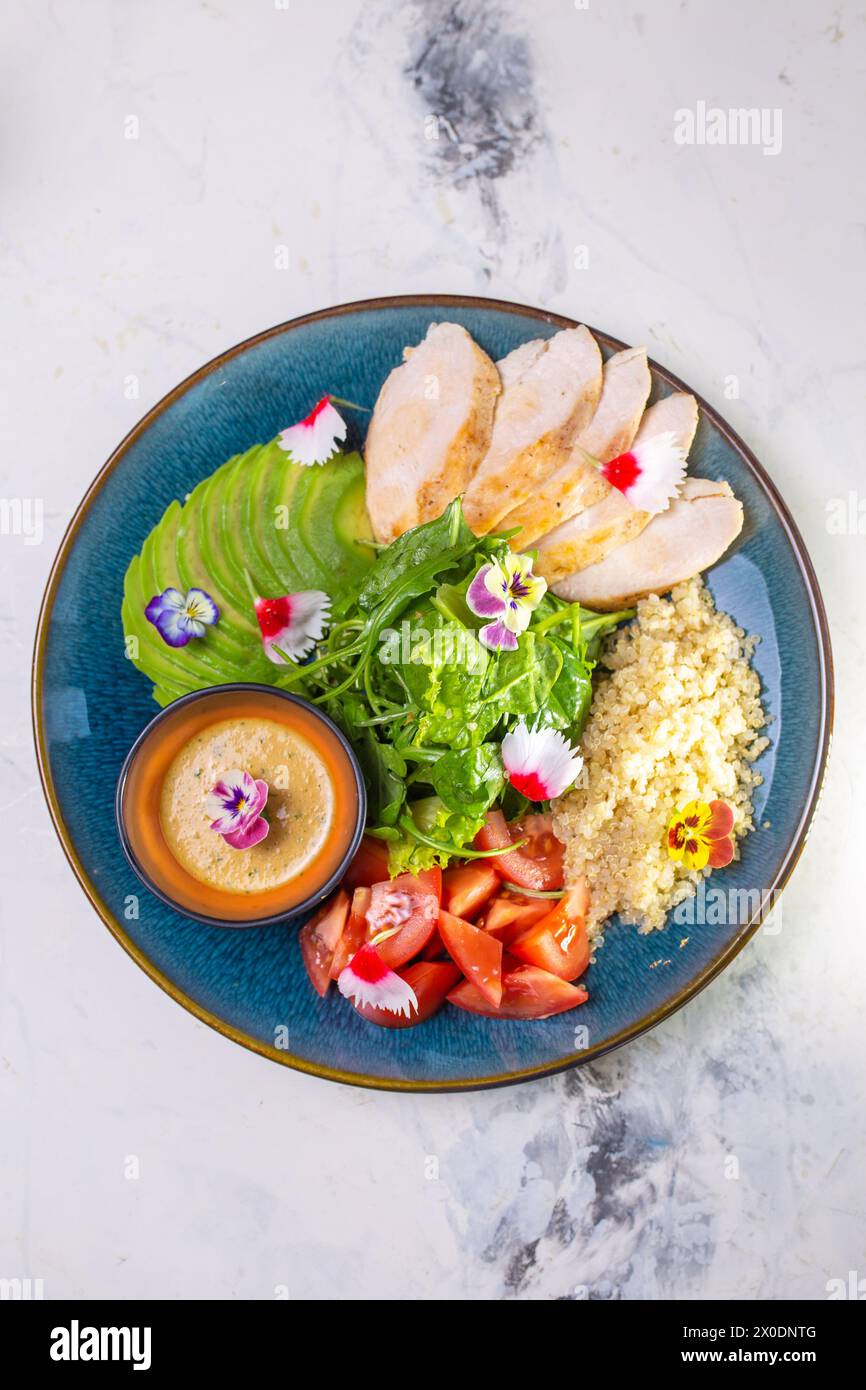 Vue de dessus du déjeuner nutritif avec poulet grillé, salade, tomates, avocat, sauce couscous sur plaque bleue. Banque D'Images