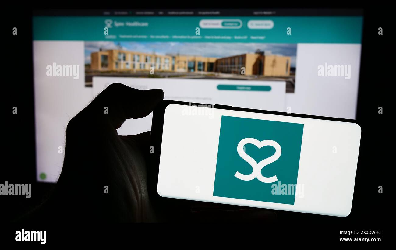 Personne tenant un smartphone avec le logo de la société britannique de santé Spire Healthcare Group plc en face du site Web. Concentrez-vous sur l'affichage du téléphone. Banque D'Images