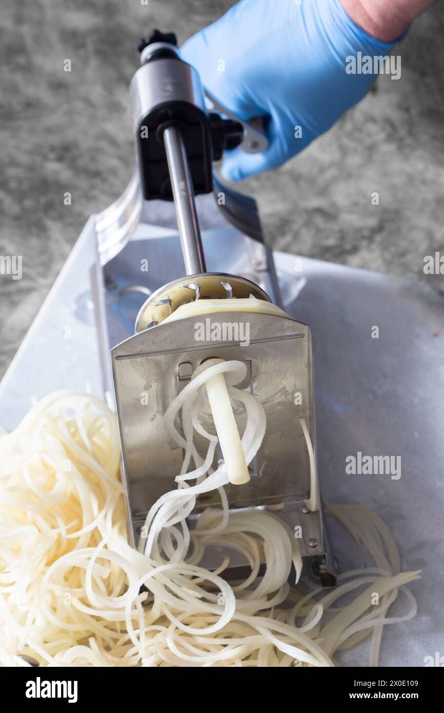 Homme utilisant le spiralizer pour couper la pomme de terre en lanières. Sur un fond de pierre sombre Banque D'Images