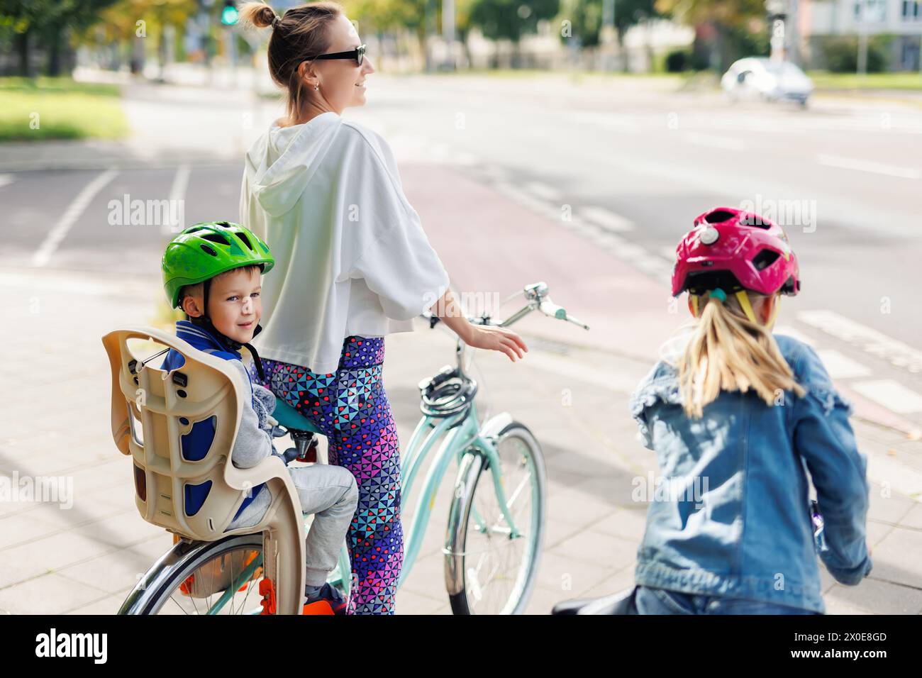 Souriante famille heureuse profiter de vélo dans les rues de la ville d'Europe par jour ensoleillé lumineux. Maman avec enfants à vélo au parc de la ville. Sièges d'enfant dans la sécurité bébé Banque D'Images