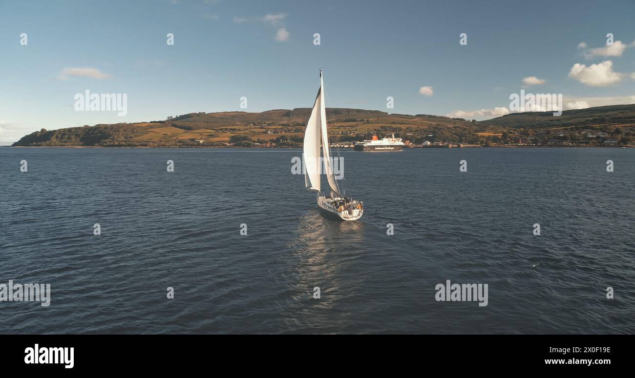 Mouvement lent de réflexion de yacht à la mer golfe aérienne. Seul bateau à voile réfléchit à Ocean Bay. Voilier de course à Brodick Harbor, Écosse, Europe. Bateau de luxe en croisière d'été. Prise de vue en lumière douce cinématographique Banque D'Images