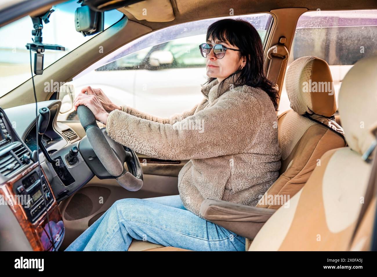 Jeune femme attrayante de 49 ans en veste regardant loin, conduisant la voiture Banque D'Images