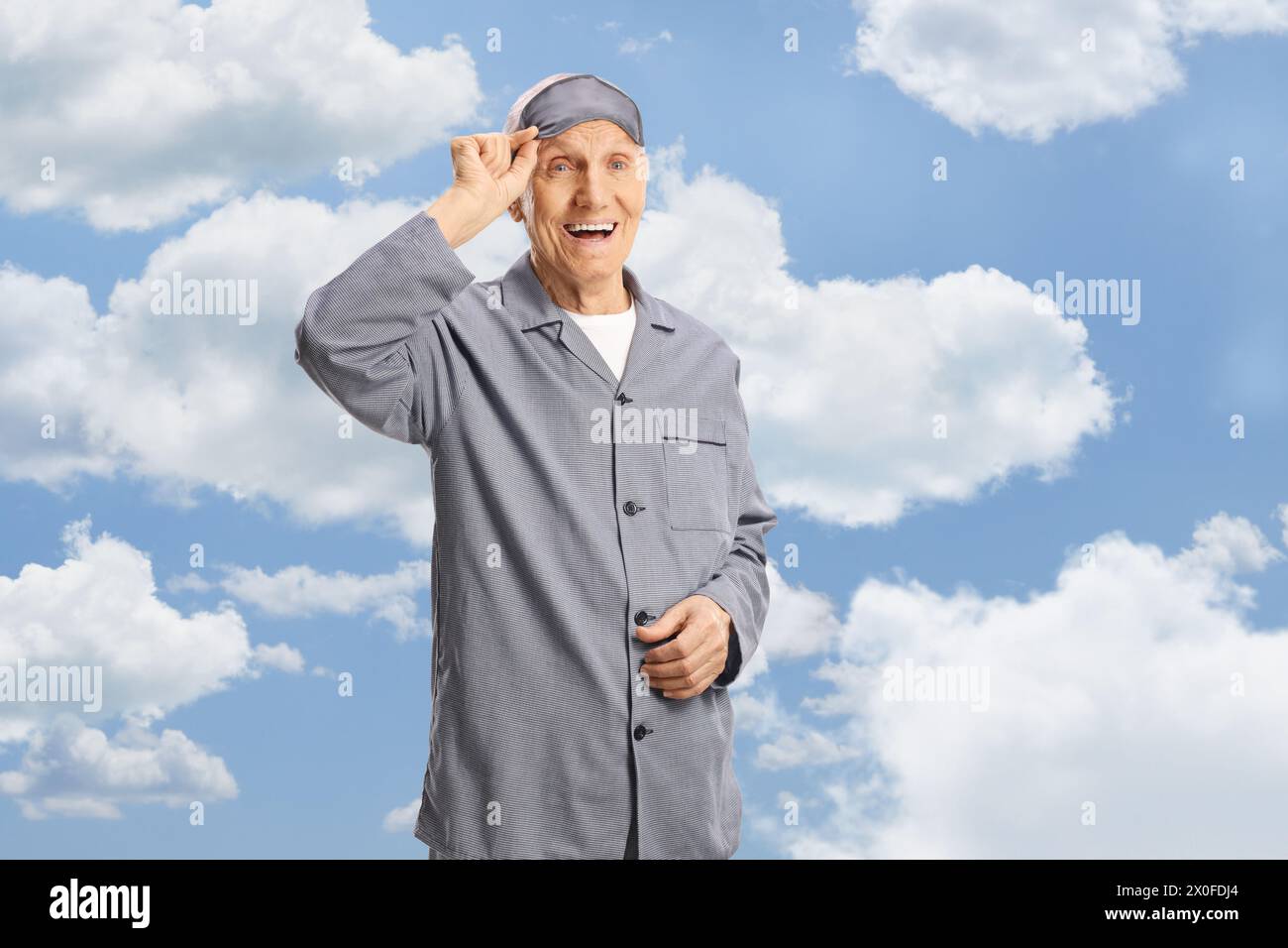 Homme âgé en pyjama enlevant un masque de sommeil entre les nuages sur un ciel bleu Banque D'Images