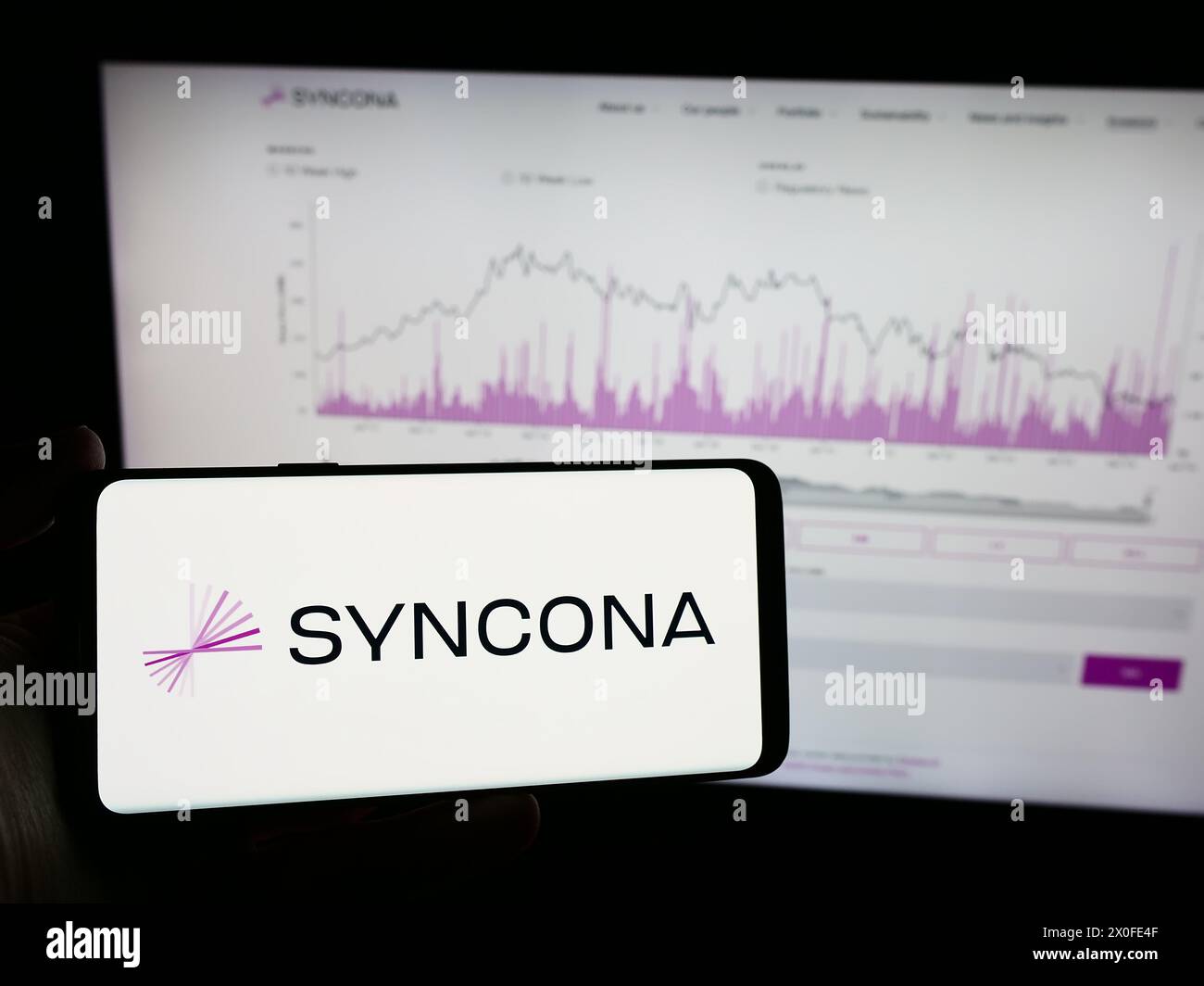 Personne tenant le téléphone portable avec le logo de la société d'investissement britannique Syncona Limited devant la page Web de l'entreprise. Concentrez-vous sur l'affichage du téléphone. Banque D'Images