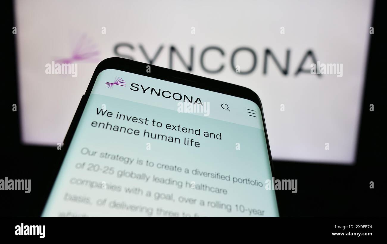 Téléphone portable avec site Web de la société d'investissement britannique Syncona Limited devant le logo de l'entreprise. Concentrez-vous sur le coin supérieur gauche de l'écran du téléphone. Banque D'Images