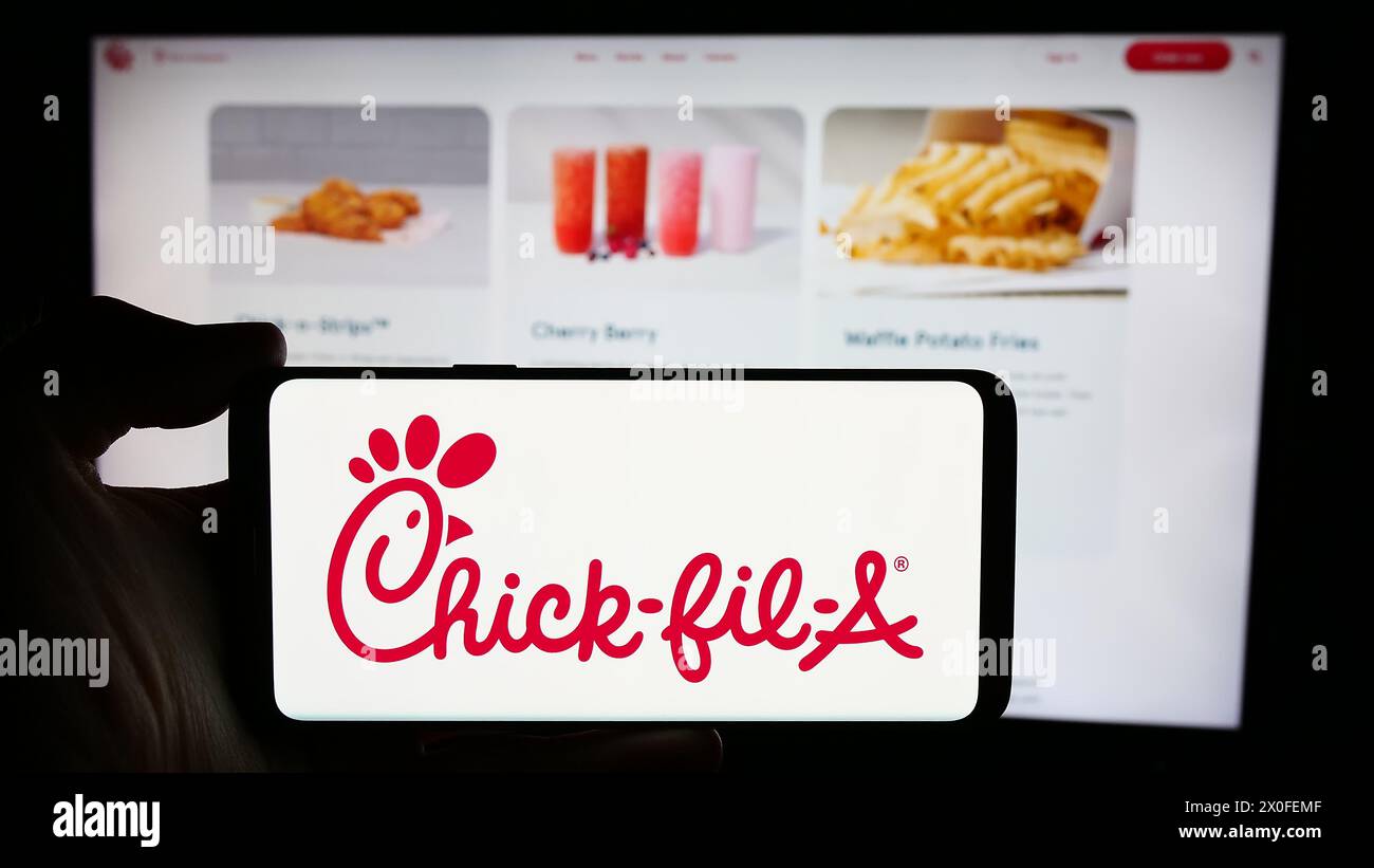 Personne tenant le téléphone portable avec le logo de la société américaine de restauration rapide Chick-fil-A Inc en face de la page Web. Concentrez-vous sur l'affichage du téléphone. Banque D'Images