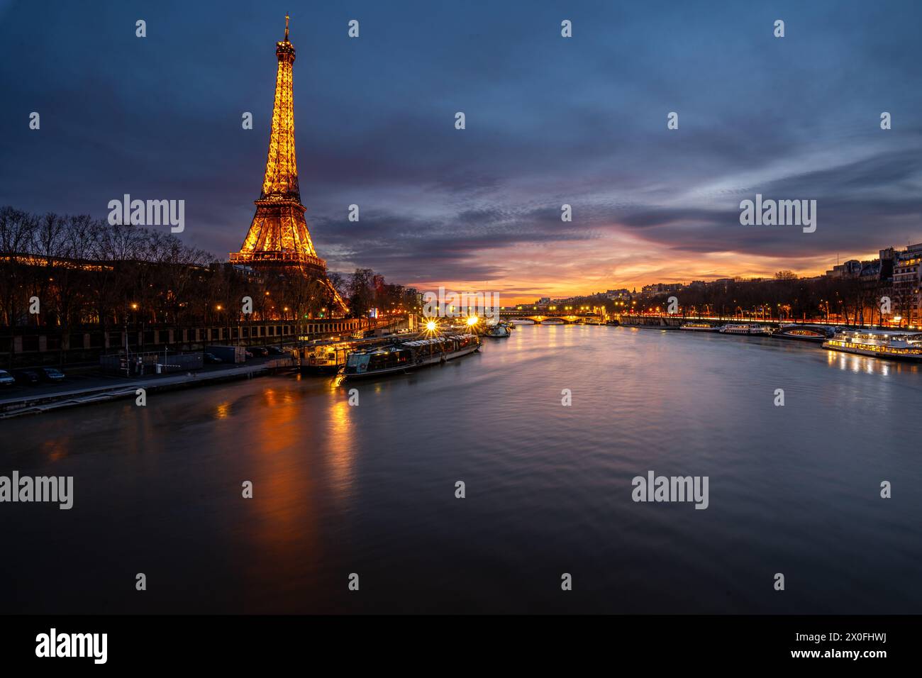 Tour Eiffel au coucher du soleil, avec le paysage urbain parisien en arrière-plan et la rivière Sena. Banque D'Images