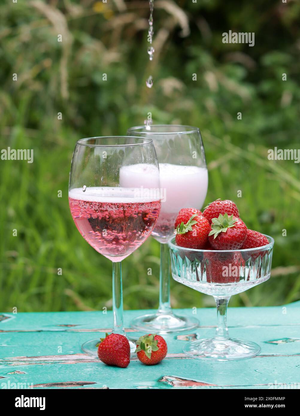 Deux verres de vin mousseux rose et fraise sur une table. Pique-nique romantique en plein air. Gros plan de la vaisselle en verre. Boissons et nourriture estivales. Banque D'Images