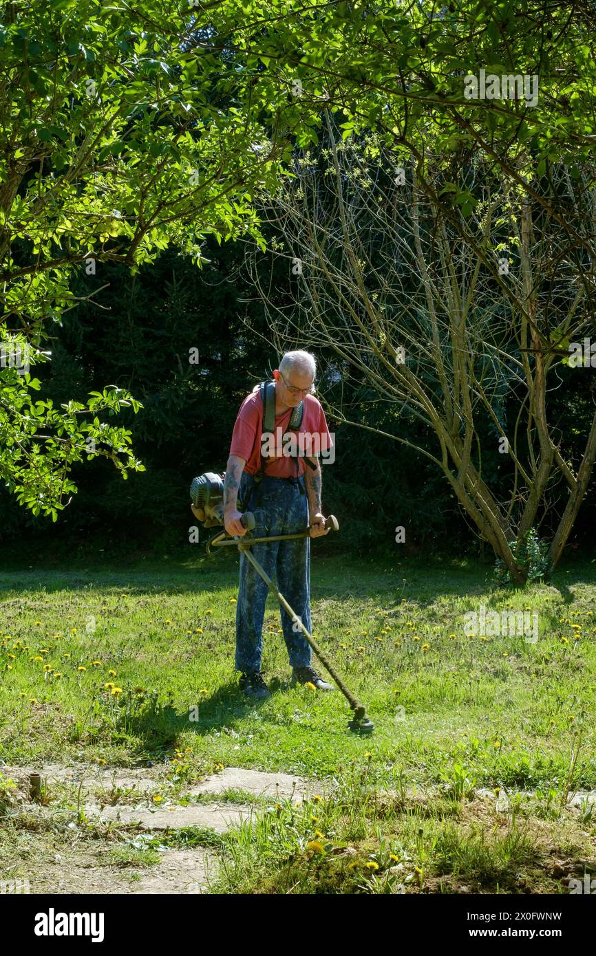homme plus âgé utilisant un débroussailleur pour couper l'herbe dans son jardin rural zala comté hongrie Banque D'Images