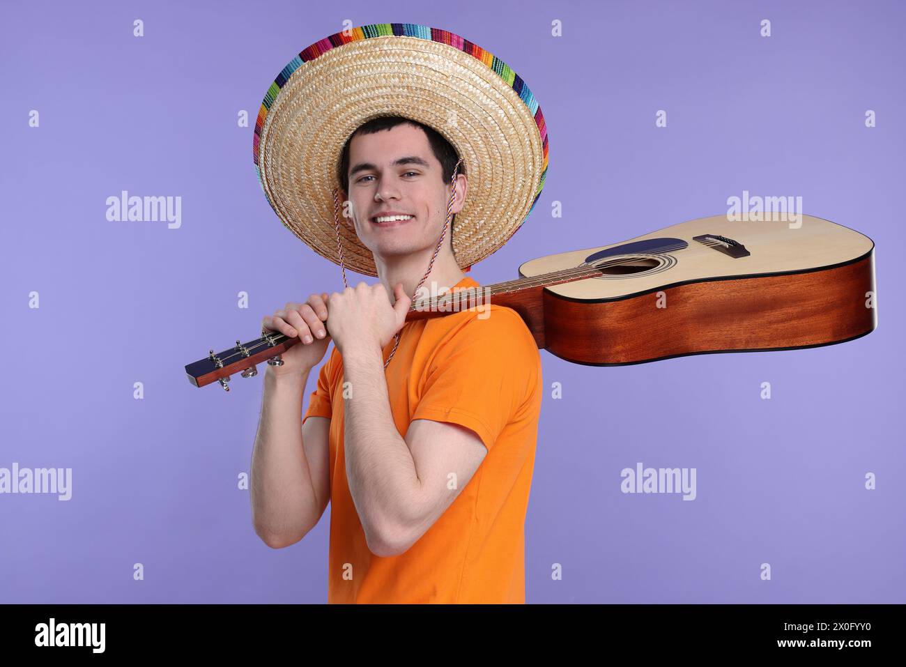 Jeune homme en chapeau sombrero mexicain avec guitare sur fond violet Banque D'Images