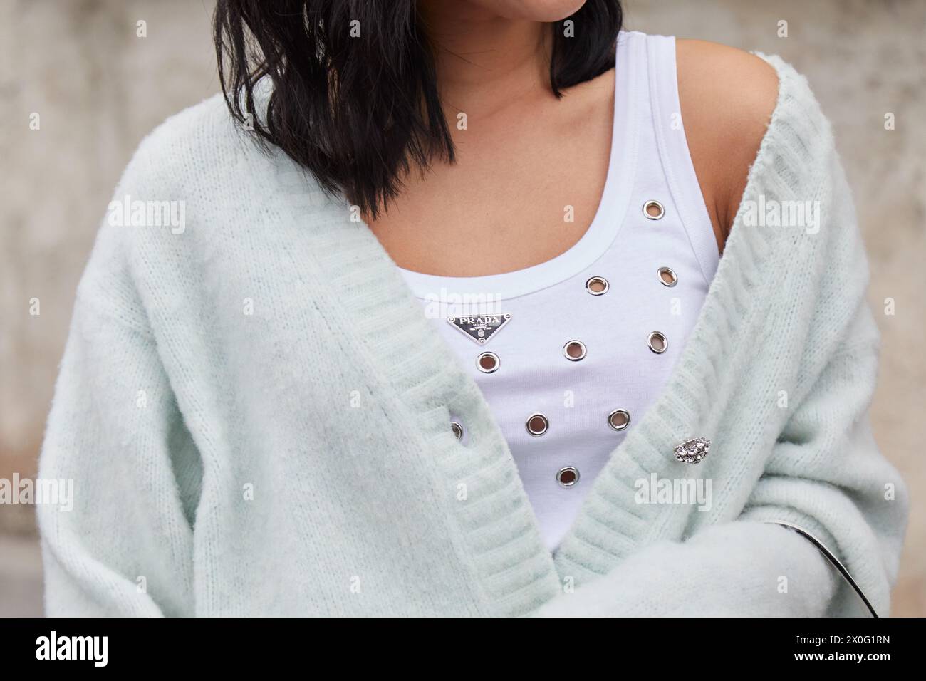 MILAN, ITALIE - 22 FÉVRIER 2024 : femme avec débardeur blanc et pull vert sauge avant le défilé de mode Prada, dans le style de rue de la semaine de la mode de Milan Banque D'Images